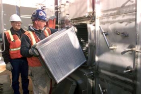 A Member of the Quality Assurance Group Watches as a Worker Installs a HEPA Filter at Silo 3.
Workers will remove 5,100 cubic yards of low-level cold metal oxide waste from Silo 3. Waste from the production process was placed in the silo between 1952 and 1957. Workers will use pneumatic and mechanical retrieval systems to remove the waste from the silo and package it in soft-sided containers for off site shipment. The waste will be treated only as required to meet commercially permitted facility's waste acceptance criteria. 
Keywords: Fernald Closure Project Fernald Green Salt Plant, Feed Materials Production Center, Fernald, Ohio (FEMP)