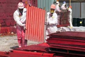 Workers Remove Transite Panels from the Pilot Plant in Preparation for the Demolition of the Concrete Structure.
The Pilot Plant was the first plant to go on line at Fernald. The plant served as an operating prototype for all phases of the uranium metal production process and a training area for new operators. Later, the plant's main function became the conversion of uranium hexaflouride (UF6) to uranium tetraflouride (UF4), called green salt, for use in the metal production process. Workers also purified thorium and converted thorium nitrate to thoria gel oxides in the plant. The D&D of the plants consists of surface decontamination, building and equipment dismantlement, size reduction of building material and the loading of demolition debris into rolloff boxes for transfer to the On-Site Disposal Facility. 
Keywords: Fernald Closure Project Fernald Green Salt Plant, Feed Materials Production Center, Fernald, Ohio (FEMP)